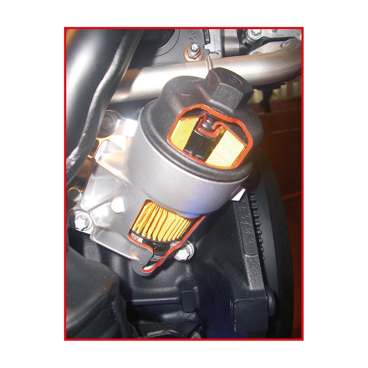 Schnitt durch einen Ölfilter, Innenleben erkennbar. Gelbes Filtermedium, rote Dichtungen, schwarzer Deckel und Metallgehäuse.